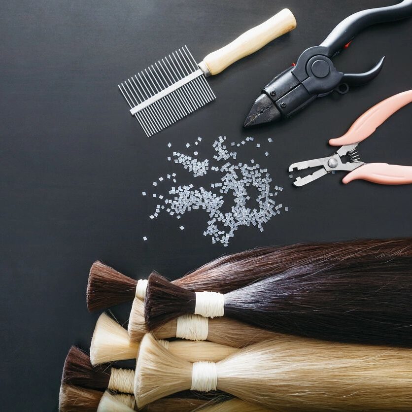 Hair cutting tools beside a bunch of different colored hair extensions
